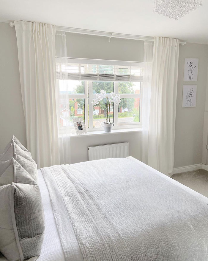big bed near the window with white curtains in a white bedroom big bed near the window with white curtains in a white bedroom