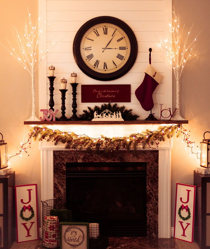Christmas themed fireplace mantel decorated with garlands, stockings, candles, and a large black and white clock above. Christmas themed fireplace mantel decorated with garlands, stockings, candles, and a large black and white clock above.