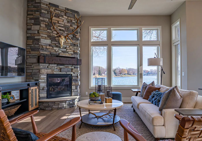 Stone accent wall fireplace mantel with large moose antlers in a cozy living room overlooking a lake view. Stone accent wall fireplace mantel with large moose antlers in a cozy living room overlooking a lake view.