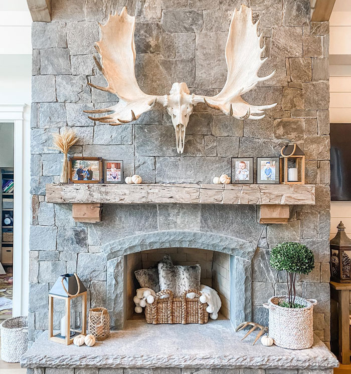 Stone living room fireplace mantel with rustic wood beam, moose antlers, and cozy decorative accents. Stone living room fireplace mantel with rustic wood beam, moose antlers, and cozy decorative accents.