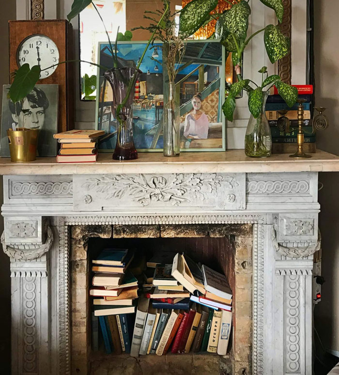 Antique fireplace mantel filled with books inside, topped with plants, artwork, and decorative items for a cozy hearth. Antique fireplace mantel filled with books inside, topped with plants, artwork, and decorative items for a cozy hearth.