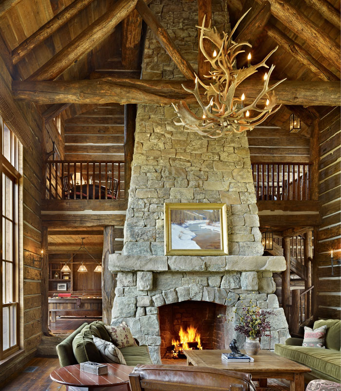Large stone fireplace with big stone mantel in rustic living room featuring antler chandelier and cozy seating area. Large stone fireplace with big stone mantel in rustic living room featuring antler chandelier and cozy seating area.