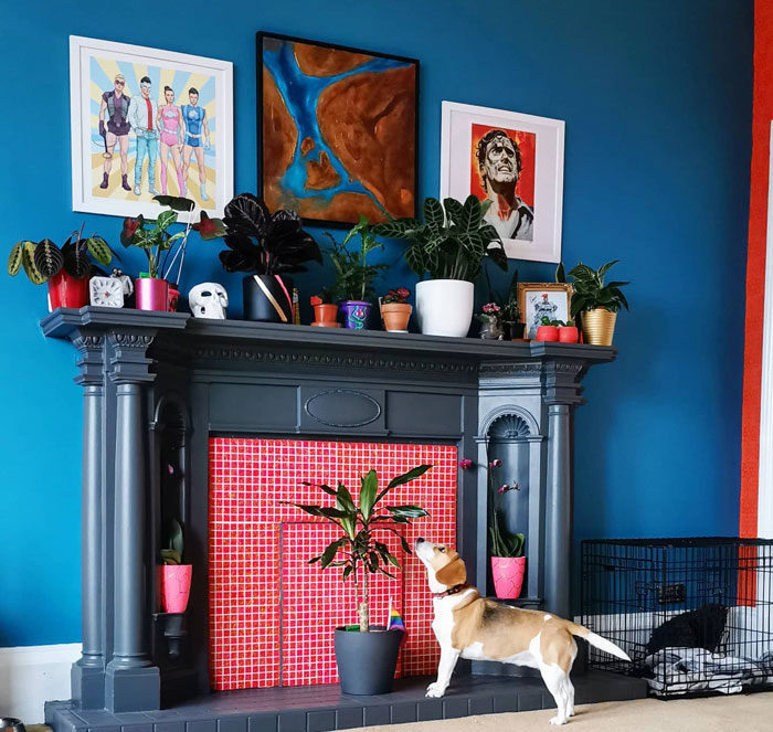 Blue living room with a dark gray fireplace mantle, potted plants and a dog