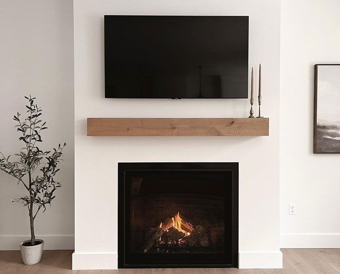 Minimalist white living room fireplace with a simple wooden mantel and TV 