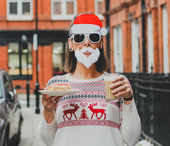 Woman wearing Christmas sweater and holding filled cup and pastry 