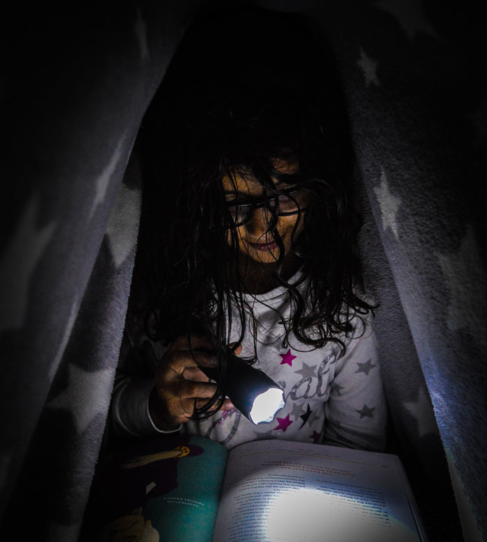 Girl under the blanket reading by flashlight 