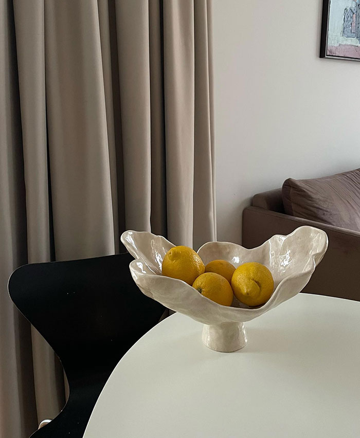 Four lemons arranged in a handmade ceramic bowl on a white table showcasing modern home decor ideas. Four lemons arranged in a handmade ceramic bowl on a white table showcasing modern home decor ideas.