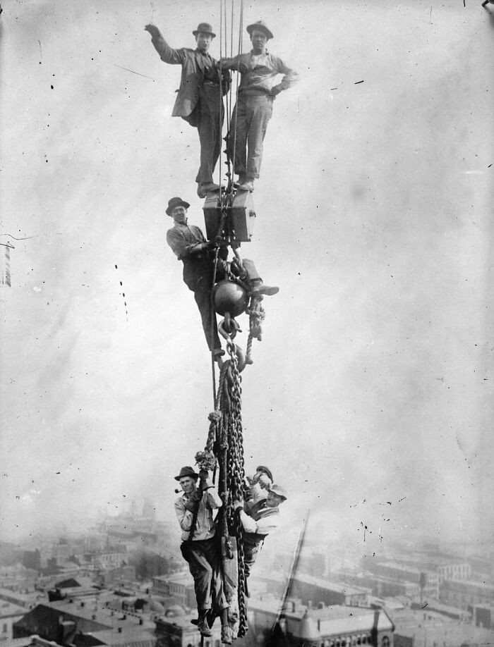 Construction Workmen Cling To Chains As They Dangle In Mid-Air Off The Side Of A Skyscraper, 1920s