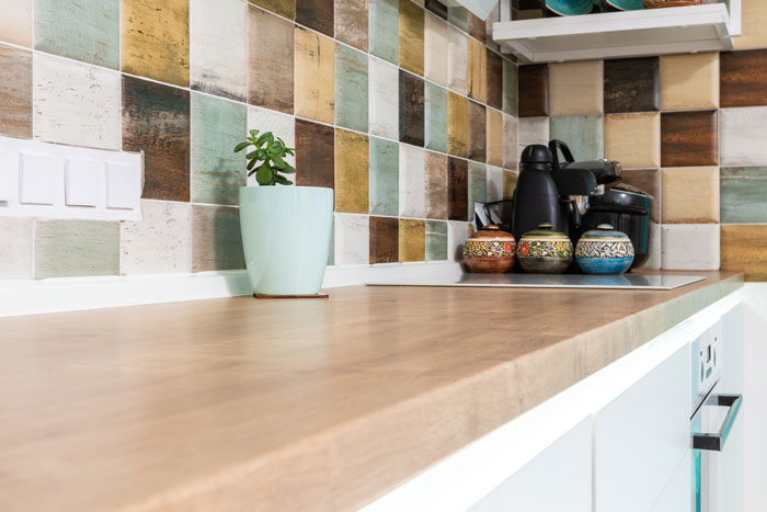 light kitchen furnished with wooden counter with multicolored tiled backsplash 