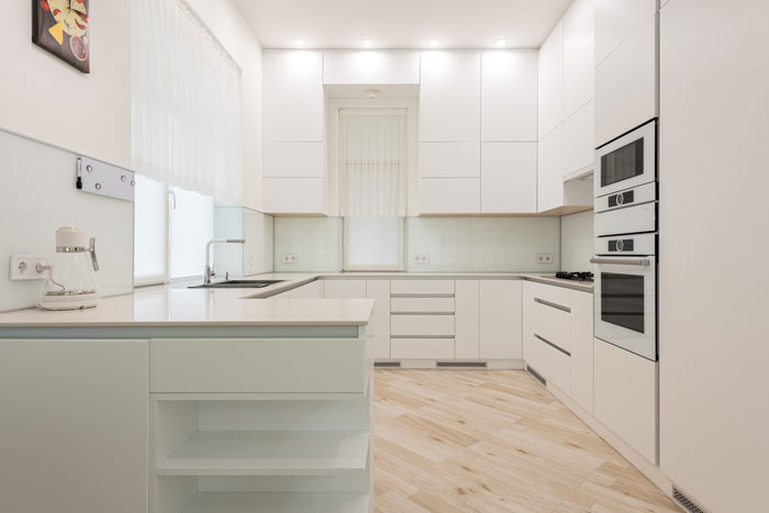 light kitchen with white cabinets and kettle near sink 
