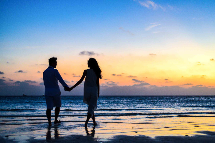 Man and woman holding hands walking on seashore during sunrise