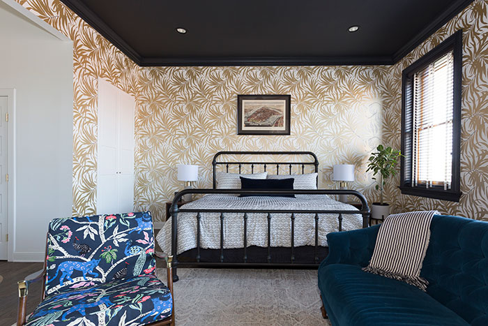 Colorful master bedroom with iron bed frame, patterned wallpaper, velvet sofa, and vibrant accent chair showcasing master bedroom ideas. Colorful master bedroom with iron bed frame, patterned wallpaper, velvet sofa, and vibrant accent chair showcasing master bedroom ideas.