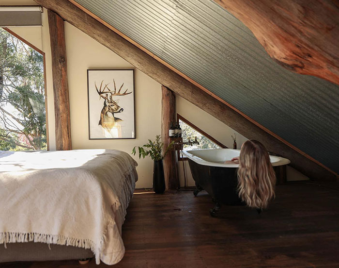 Clawfoot tub placed in a master bedroom with slanted ceiling and rustic wood beams, showcasing unique master bedroom ideas. Clawfoot tub placed in a master bedroom with slanted ceiling and rustic wood beams, showcasing unique master bedroom ideas.