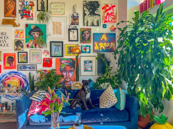 a maximalist living room with a dog sitting on a blue couch and many pictures on the wall