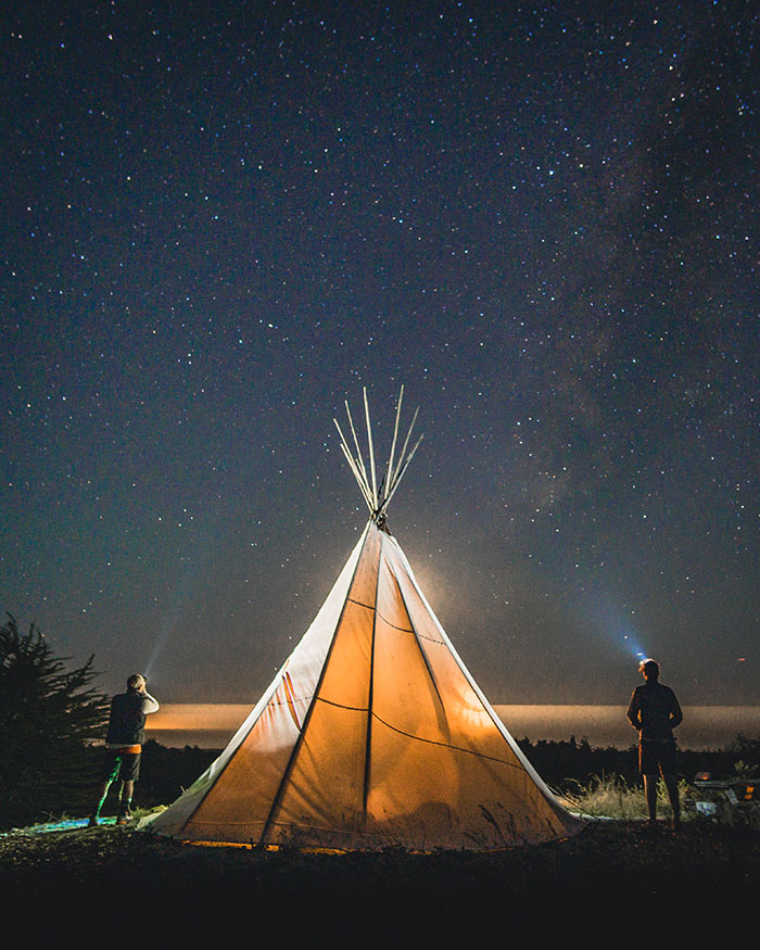 Two persons standing beside tipis during nighttime.