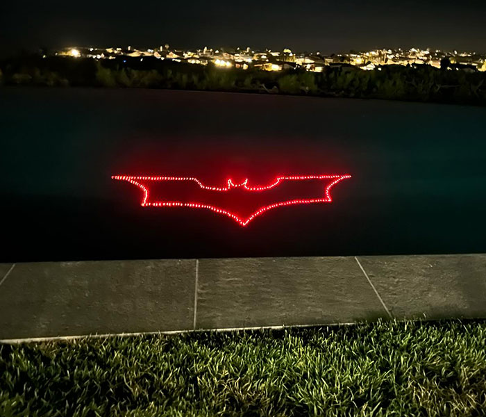 Red Batman logo glowing against a city nightscape backdrop. Red Batman logo glowing against a city nightscape backdrop.