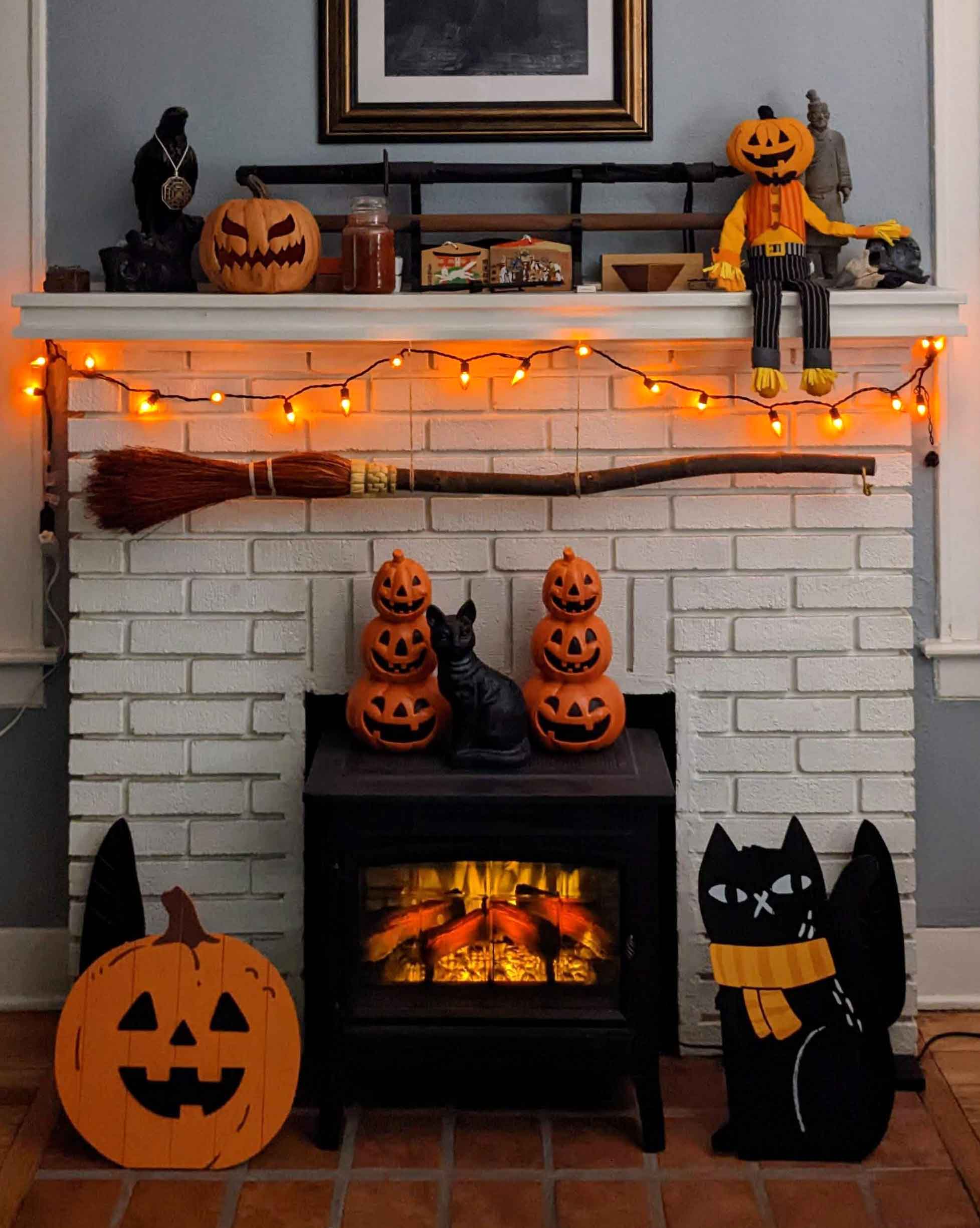 Fire place decorated with pumpkins, cats, broom and fairy lights