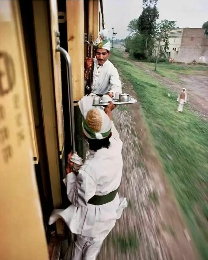 Two Men Passing Breakfast Tea From The Kitchen Car On A Moving Train, Due To A Door Being Locked Between The Train Cars, On A Railway From Peshawar To Rawalpindi, Pakistan, 1983. Photo By Steve Mccurry