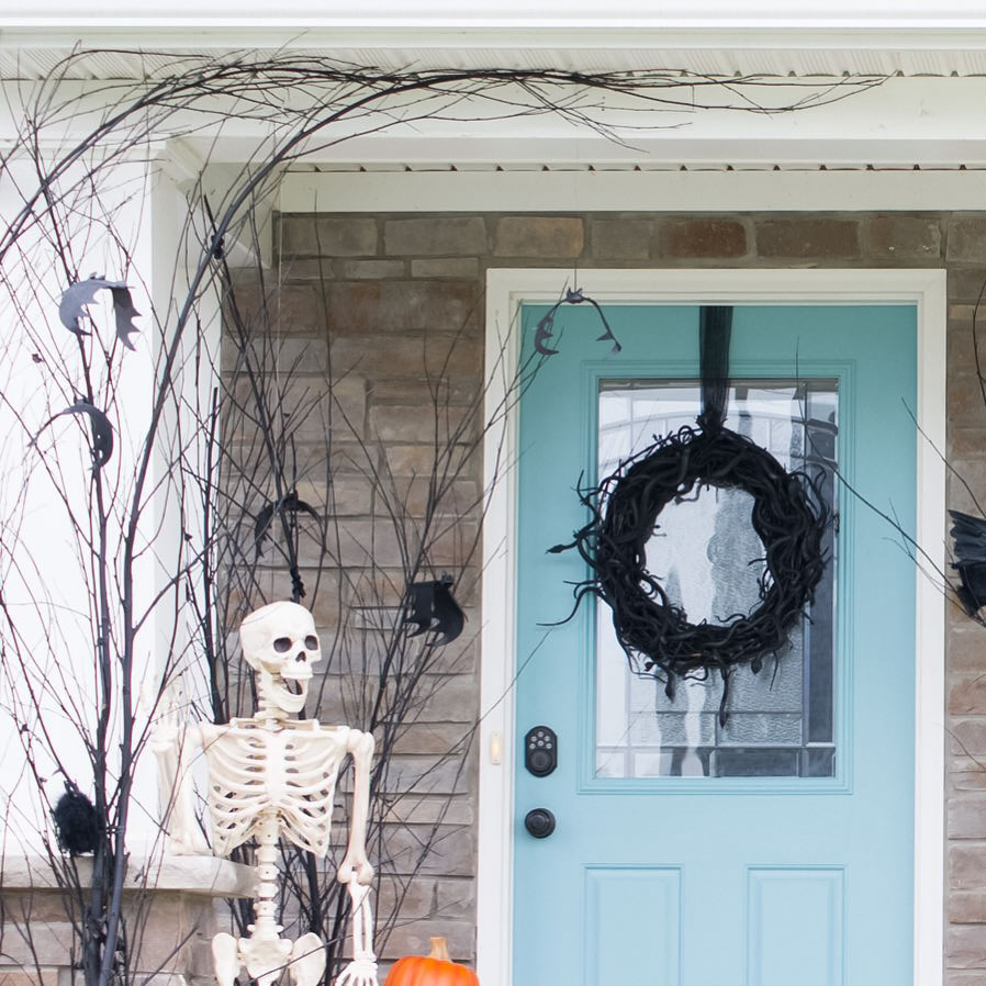 A porch decorated with branches,  skeleton and wreath
