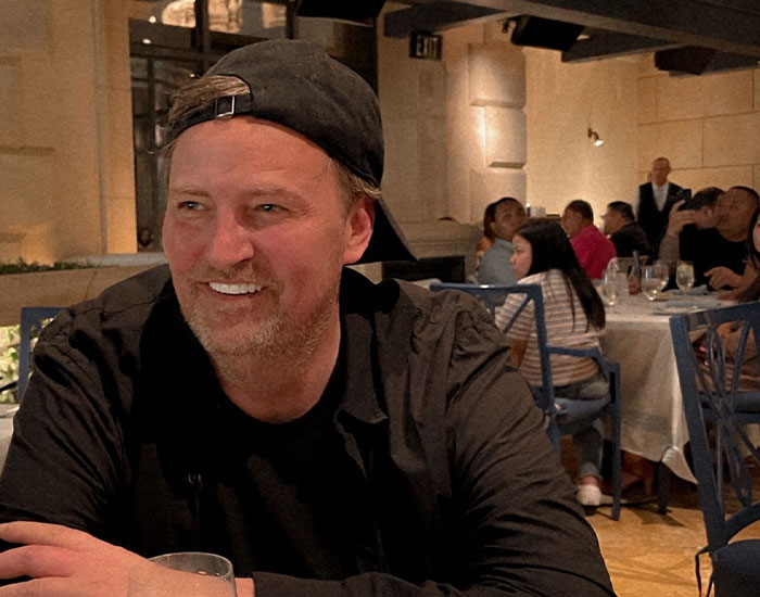 Man in a restaurant wearing a black shirt and hat, smiling among diners, related to mysterious Batman-themed posts. Man in a restaurant wearing a black shirt and hat, smiling among diners, related to mysterious Batman-themed posts.