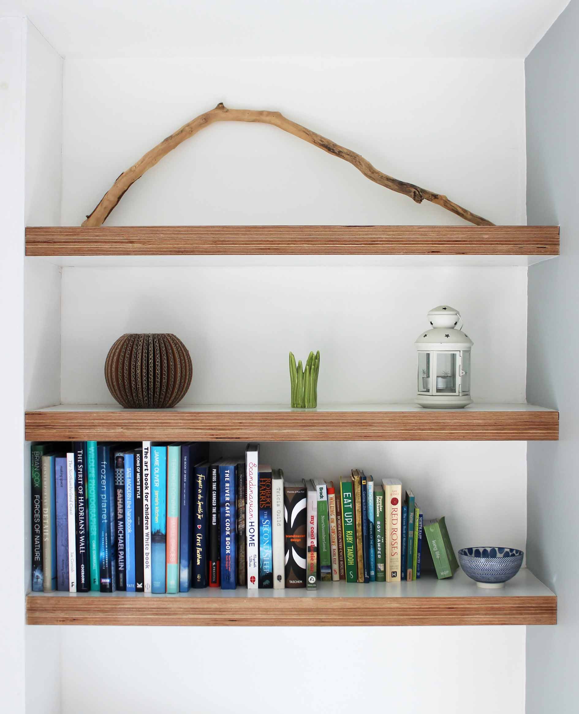 Three wooden shelves with books and a tree stick