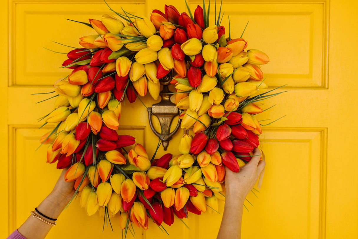 Woman hanging a tulip wreath on a yellow door