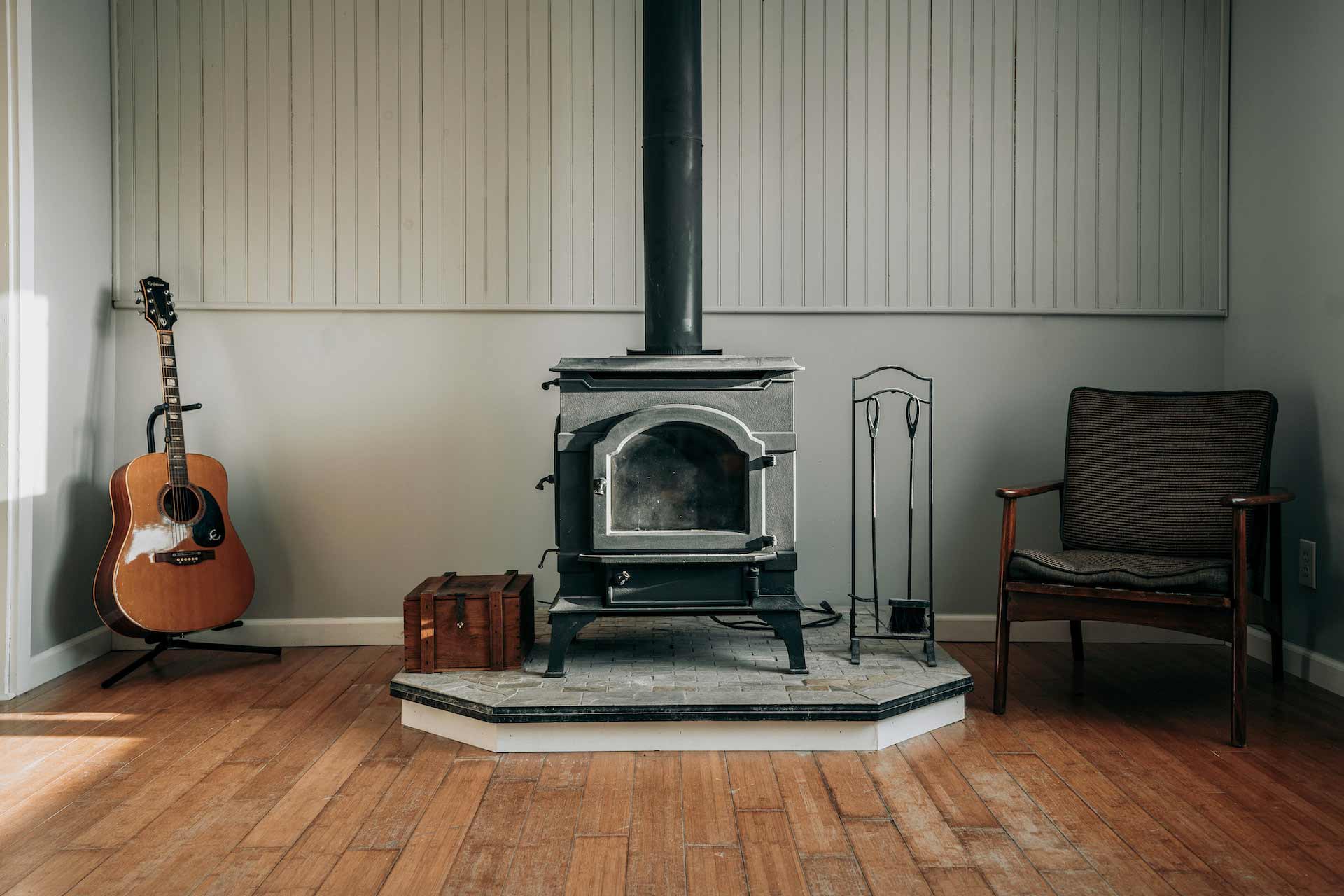 A room with a wood-burning stove, a guitar, and an armchair
