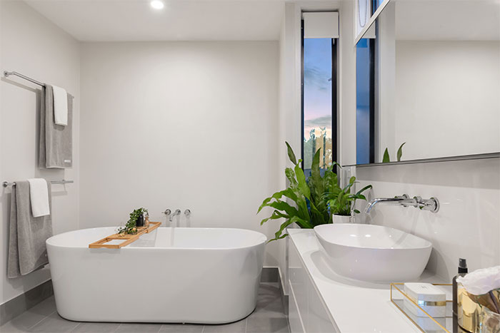 all-white bathroom with ceramic bathtub near green potted plant