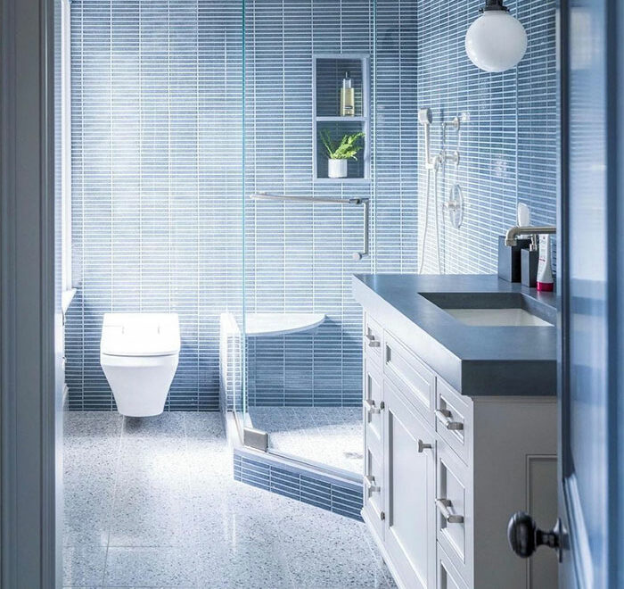 blue bathroom with small blue rectangular tiles with white cabinets 