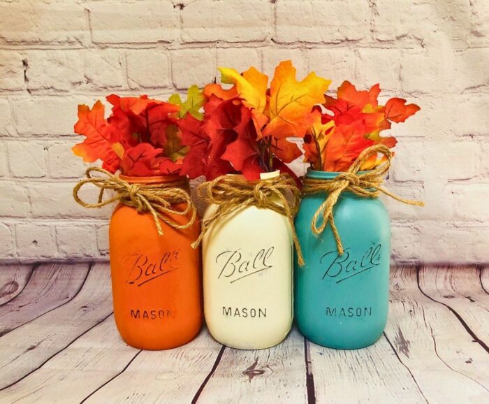 Orange, white, and blue chalk-painted mason jars with maple leaves in them