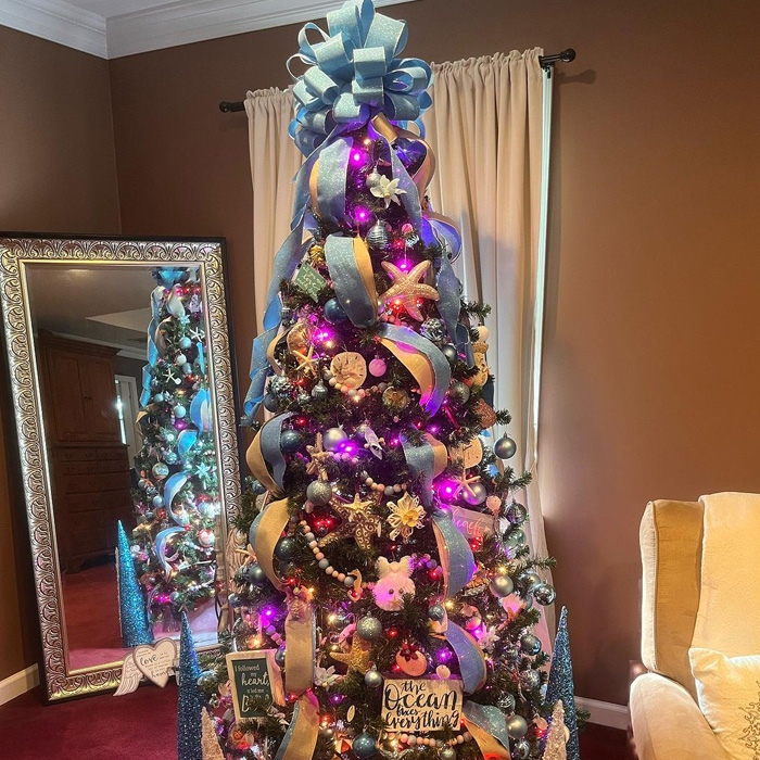 Decorated Christmas tree with a blue bow as a toping and seashells ornaments 
