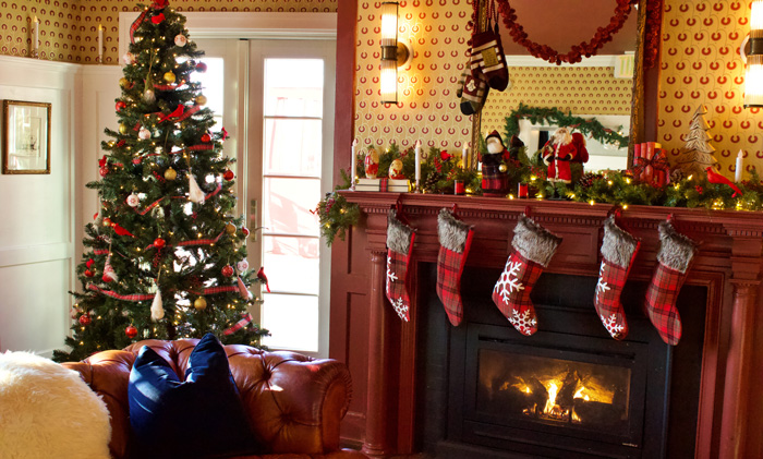 Decorated Christmas tree next to a fireplace with stockings on it 