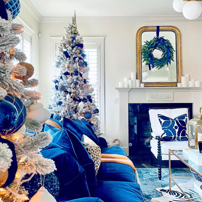 Silver Christmas tree decorated with blue ornaments next to a blue couch 