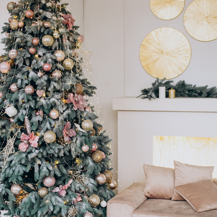 Decorated Christmas tree with boxes under it next to a pale pink couch 