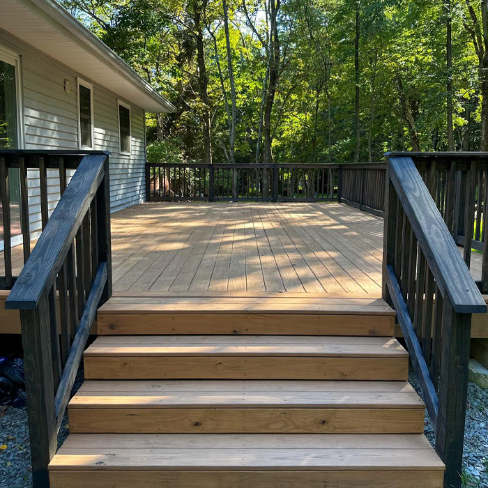 Raised backyard deck with wooden stairs and black railings surrounded by trees, showcasing creative backyard deck ideas. Raised backyard deck with wooden stairs and black railings surrounded by trees, showcasing creative backyard deck ideas.