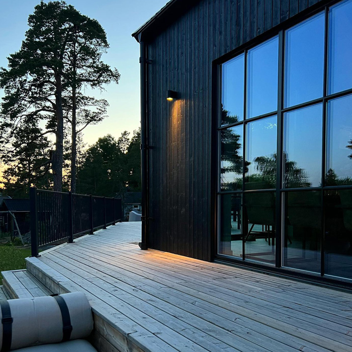 Spacious backyard deck wrapping around the house with outdoor lighting and large windows reflecting trees at dusk Spacious backyard deck wrapping around the house with outdoor lighting and large windows reflecting trees at dusk
