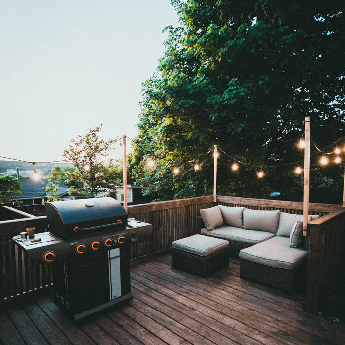 Black grill and cozy seating on a wooden backyard deck with string lights creating a warm outdoor ambiance. Black grill and cozy seating on a wooden backyard deck with string lights creating a warm outdoor ambiance.