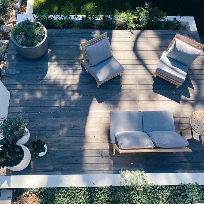 Wooden outdoor furniture with cushions and plants on a backyard deck showcasing creative backyard deck ideas. Wooden outdoor furniture with cushions and plants on a backyard deck showcasing creative backyard deck ideas.