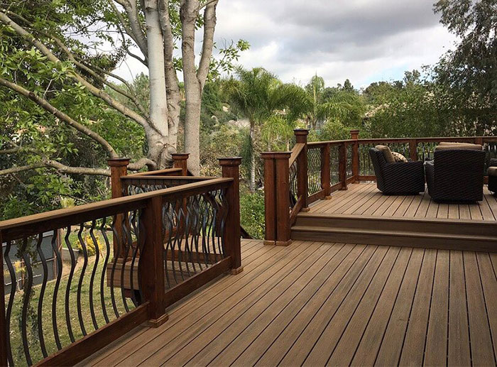 Wooden deck featuring arced black metal deck railings surrounded by trees and outdoor seating area. Wooden deck featuring arced black metal deck railings surrounded by trees and outdoor seating area.