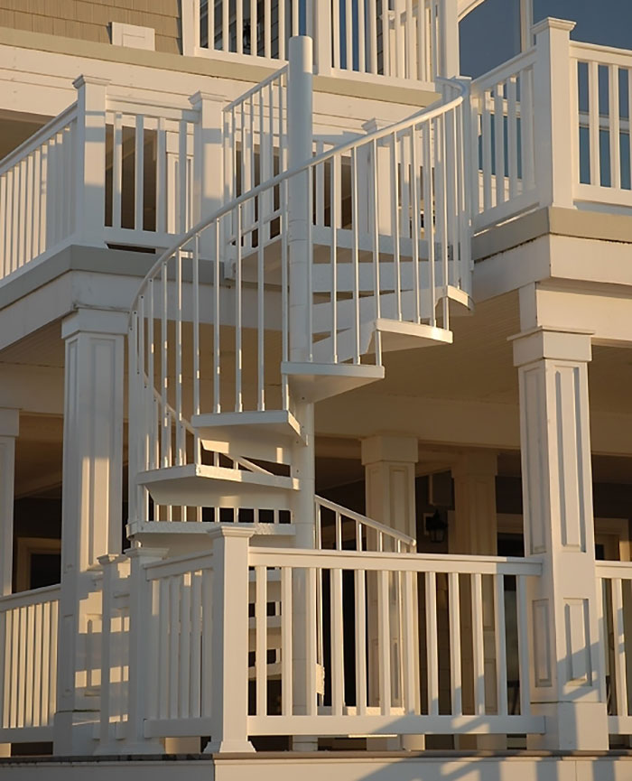White snaking up and down deck railing design featuring a spiral staircase with vertical balusters and posts. White snaking up and down deck railing design featuring a spiral staircase with vertical balusters and posts.