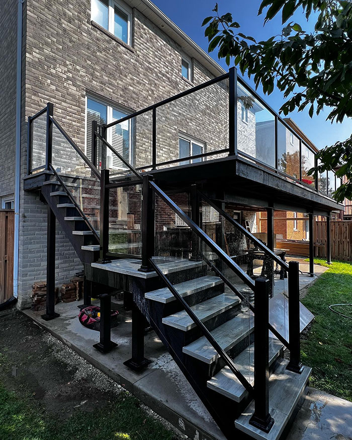 Modern multi-panel glass deck railing with black frames enhancing exterior design and safety on outdoor stairs and balcony. Modern multi-panel glass deck railing with black frames enhancing exterior design and safety on outdoor stairs and balcony.