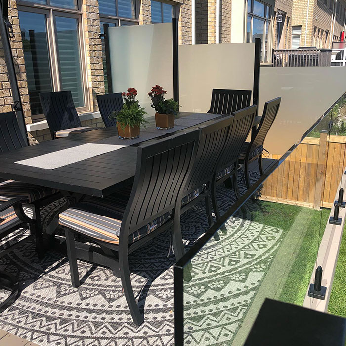Patio with frosted glass deck railing and black outdoor dining table with chairs on patterned rug. Patio with frosted glass deck railing and black outdoor dining table with chairs on patterned rug.