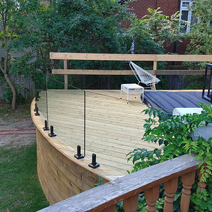 Curved wooden deck with sleek single-panel glass deck railing design for a modern exterior look. Curved wooden deck with sleek single-panel glass deck railing design for a modern exterior look.