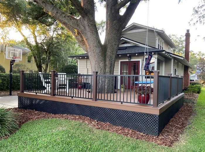Wooden and metal deck railings surrounding a raised deck area near a house with outdoor seating and greenery. Wooden and metal deck railings surrounding a raised deck area near a house with outdoor seating and greenery.