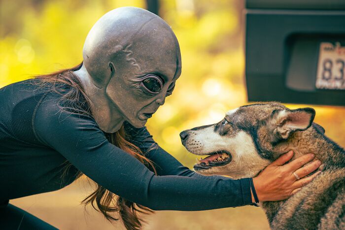 woman wearing alien mask hugging dog