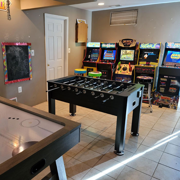 Game room with air hockey and foosball tables, arcade machines, and colorful stools in a vibrant gaming cave setup. Game room with air hockey and foosball tables, arcade machines, and colorful stools in a vibrant gaming cave setup.