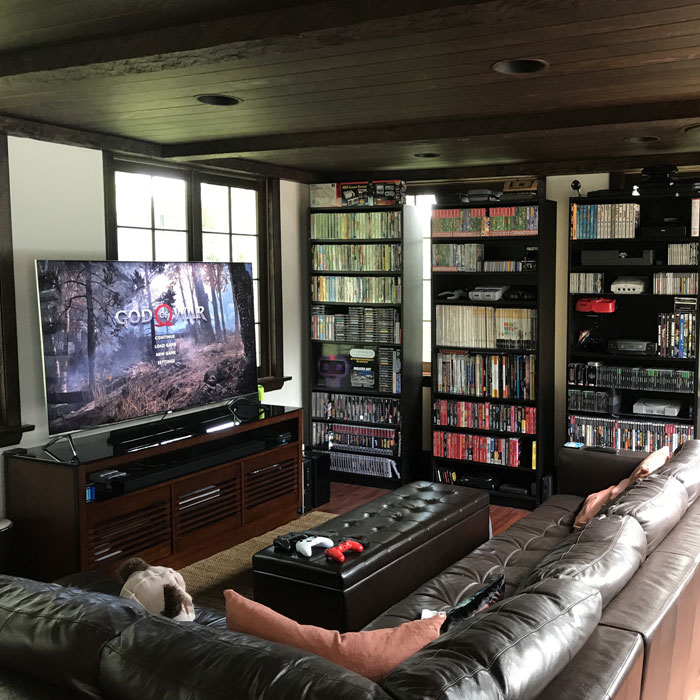 Game room in a living room with large TV, gaming consoles, shelf filled with games, and comfortable leather seating area Game room in a living room with large TV, gaming consoles, shelf filled with games, and comfortable leather seating area