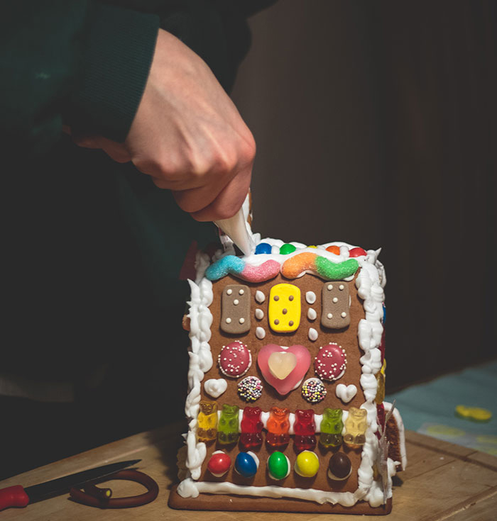 A person decorating a gingerbread house with icing.