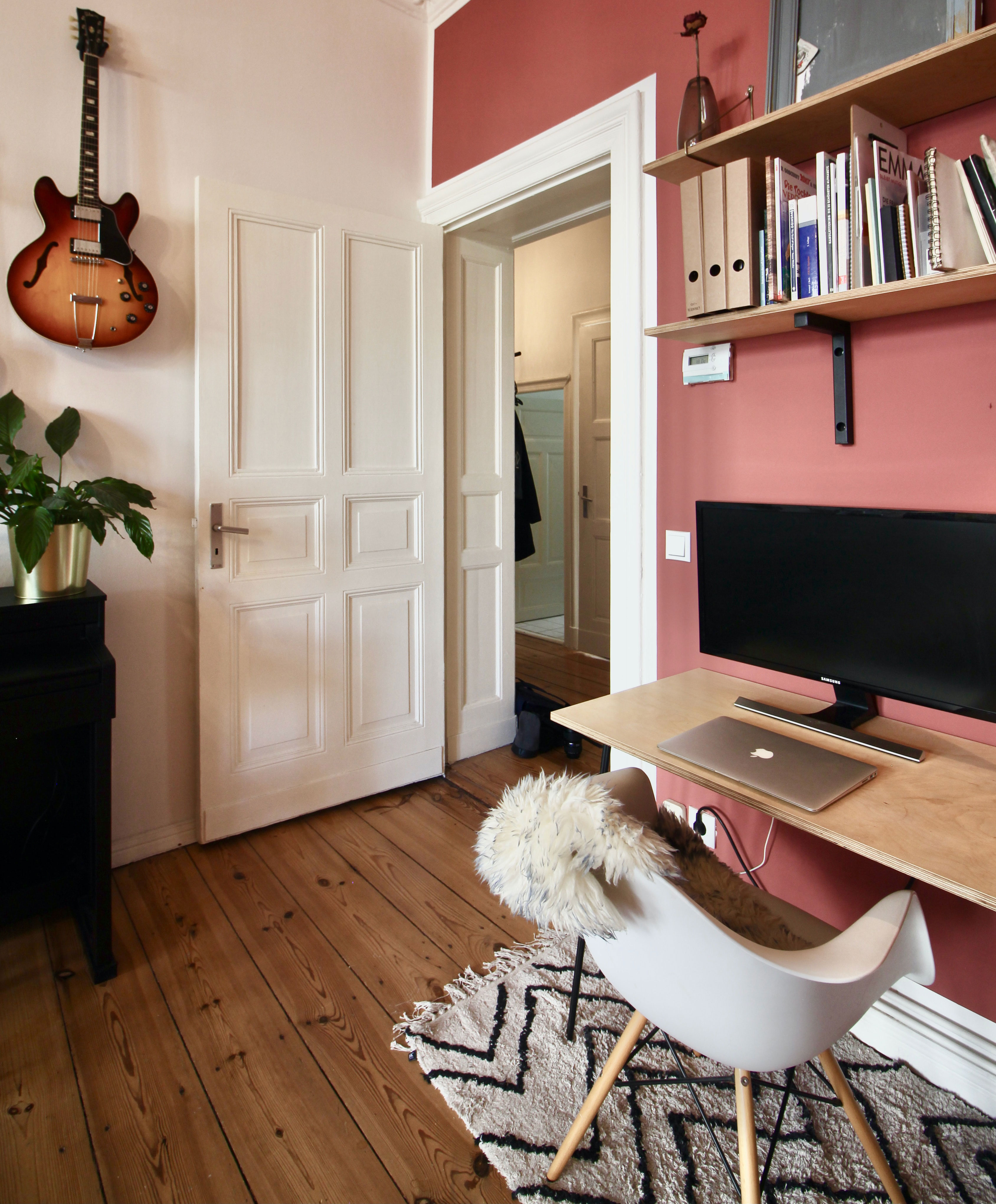 Brown acoustic guitar mounted on white wall in a stylish home office with wooden floor and productive work setup Brown acoustic guitar mounted on white wall in a stylish home office with wooden floor and productive work setup