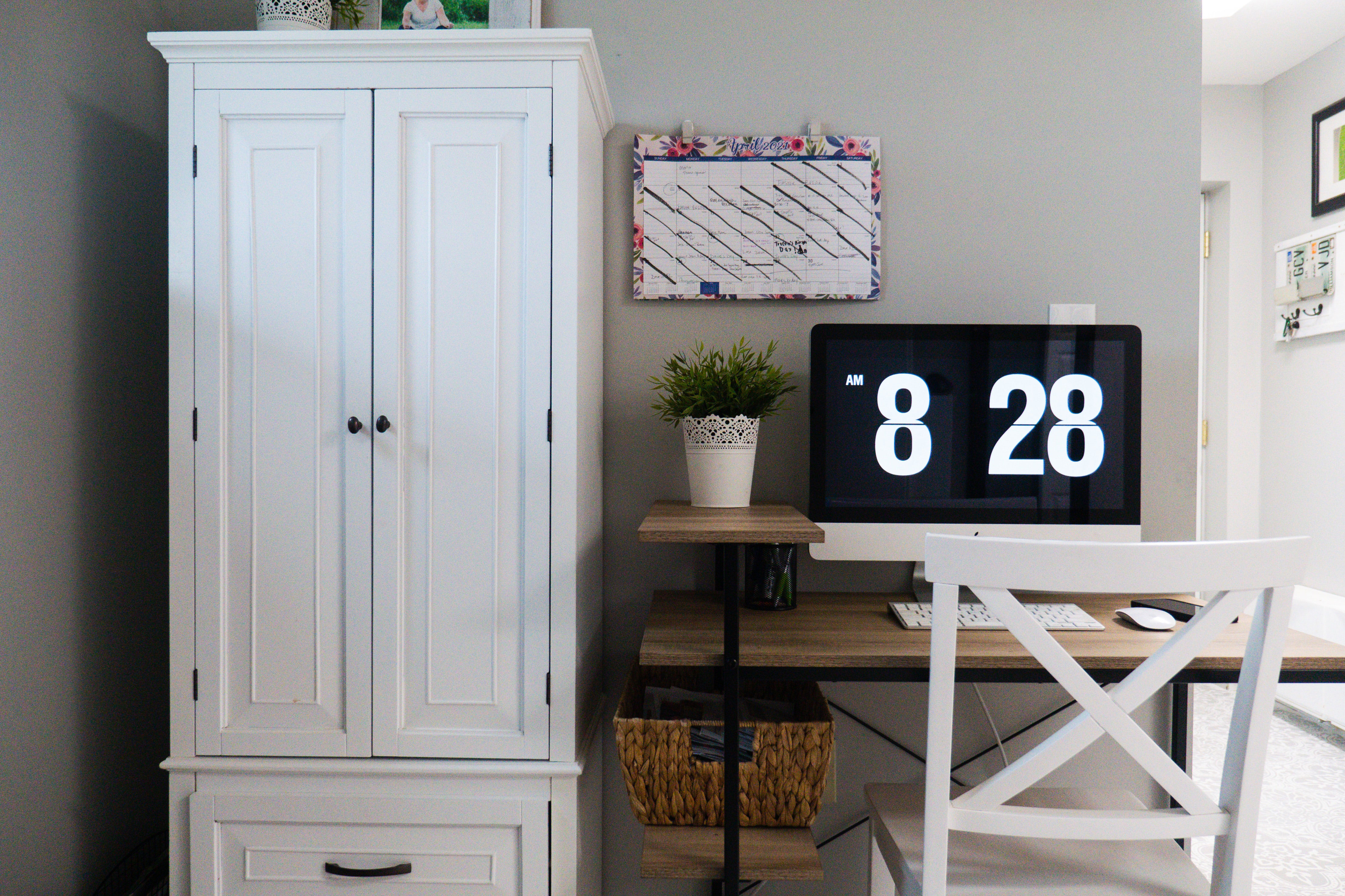 White cupboard next to wooden desk with computer and plant in a modern home office setup for productivity. White cupboard next to wooden desk with computer and plant in a modern home office setup for productivity.